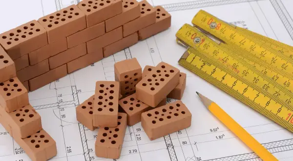 Miniaturowa budowa na planie architektonicznym: cegły, miarka i ołówek. To jakby planistyczna zabawa w budowanie.