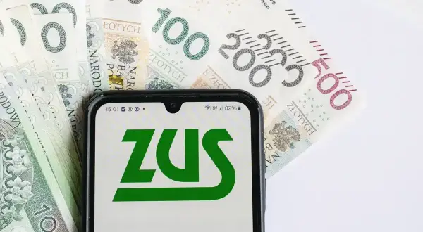 Złote banknoty i smartfon z logo ZUS. Możliwość złożenia wniosku o zasiłek pogrzebowy online.