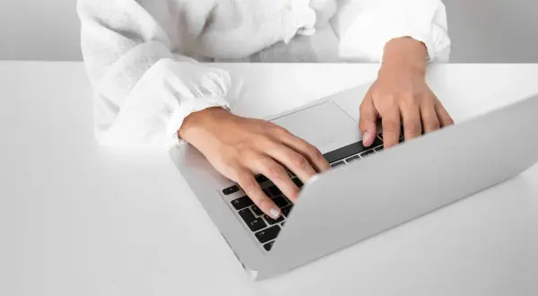Dłonie piszą na laptopie, szukając informacji o zaświadczenie o niezaleganiu ZUS.