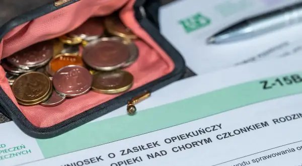 Portmonetka z monetami obok wniosku o zasiłek opiekuńczy. Dokumenty i drobne pieniądze symbolizują wsparcie finansowe dla opiekunów.