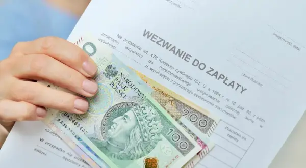 Dłoń trzyma banknoty 100 i 200 zł na wezwaniu do zapłaty. Zastanawiasz się, ile zarabia komornik?