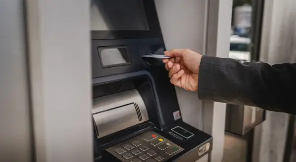 Dłoń wsuwa kartę do bankomatu, by sprawdzić, ile można wypłacić.