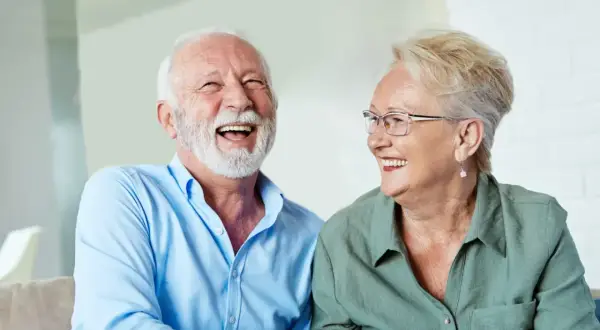 Szczęśliwi seniorzy śmieją się, omawiając zwrot podatku od 13 i 14 emerytury w tabeli.