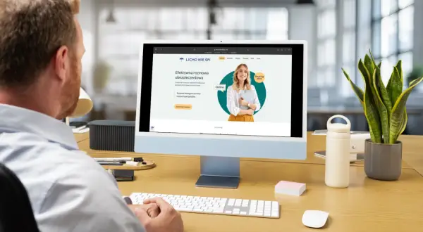 Mężczyzna pracuje przy komputerze, na ekranie którego widoczna jest strona internetowa agencji ubezpieczeniowej.