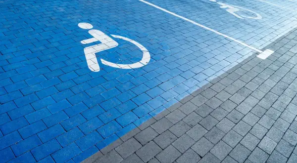 Niebieski parking z symbolem wózka inwalidzkiego. Orzeczenie o niepełnosprawności można uzyskać na wiele chorób, które ograniczają sprawność.