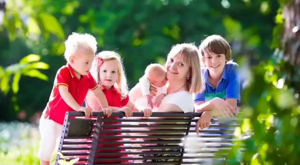 Szczęśliwa mama z czwórką dzieci na ławce w parku. Marzy o tym, kiedy emerytura dla matek 3 dzieci od kiedy będzie jej przysługiwać.