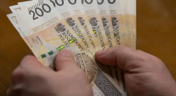 Dwie ręce trzymają plik banknotów po 200 zł. To może być wypłata 5000 brutto.