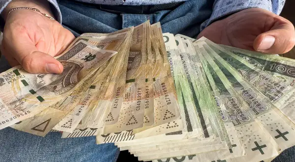 Ręce trzymające stos banknotów 100 i 200 zł. To darowizna od rodziców na nowy cel.