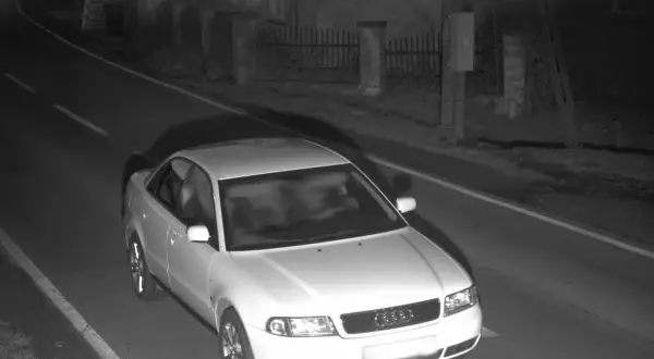 Biały sedan Audi jedzie nocą po drodze, prawdopodobnie zarejestrowany przez fotoradar.