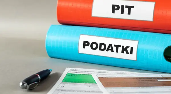 Dwa segregatory, jeden czerwony z napisem "PIT", drugi niebieski z napisem "PODATKI", leżą na dokumentach podatkowych.