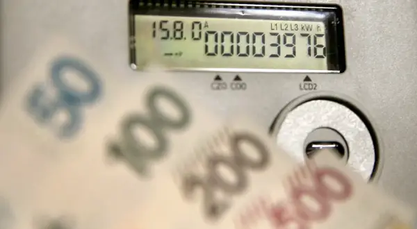 Licznik energii pokazuje zużycie 3976 kWh. W tle rozmazane banknoty 50, 100, 200, 500 zł, sugerujące wysoką cenę za kWh.