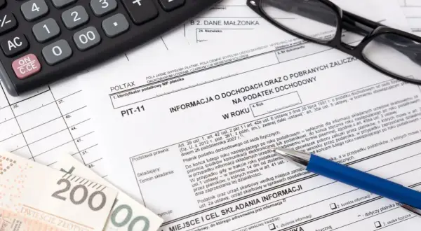 Na PIT-11 widoczne są dokumenty, kalkulator i pieniądze. Kwota zwrotu PIT-11 jest ukryta.