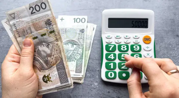Ręka trzyma banknoty 200 zł i 100 zł, obok kalkulator z wyświetloną kwotą 50000. Czy to prognoza wynagrodzenia minimalnego 2026?