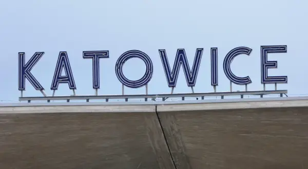 Napis "KATOWICE" z niebieskimi neonami na tle jasnego nieba, nad betonową konstrukcją.
