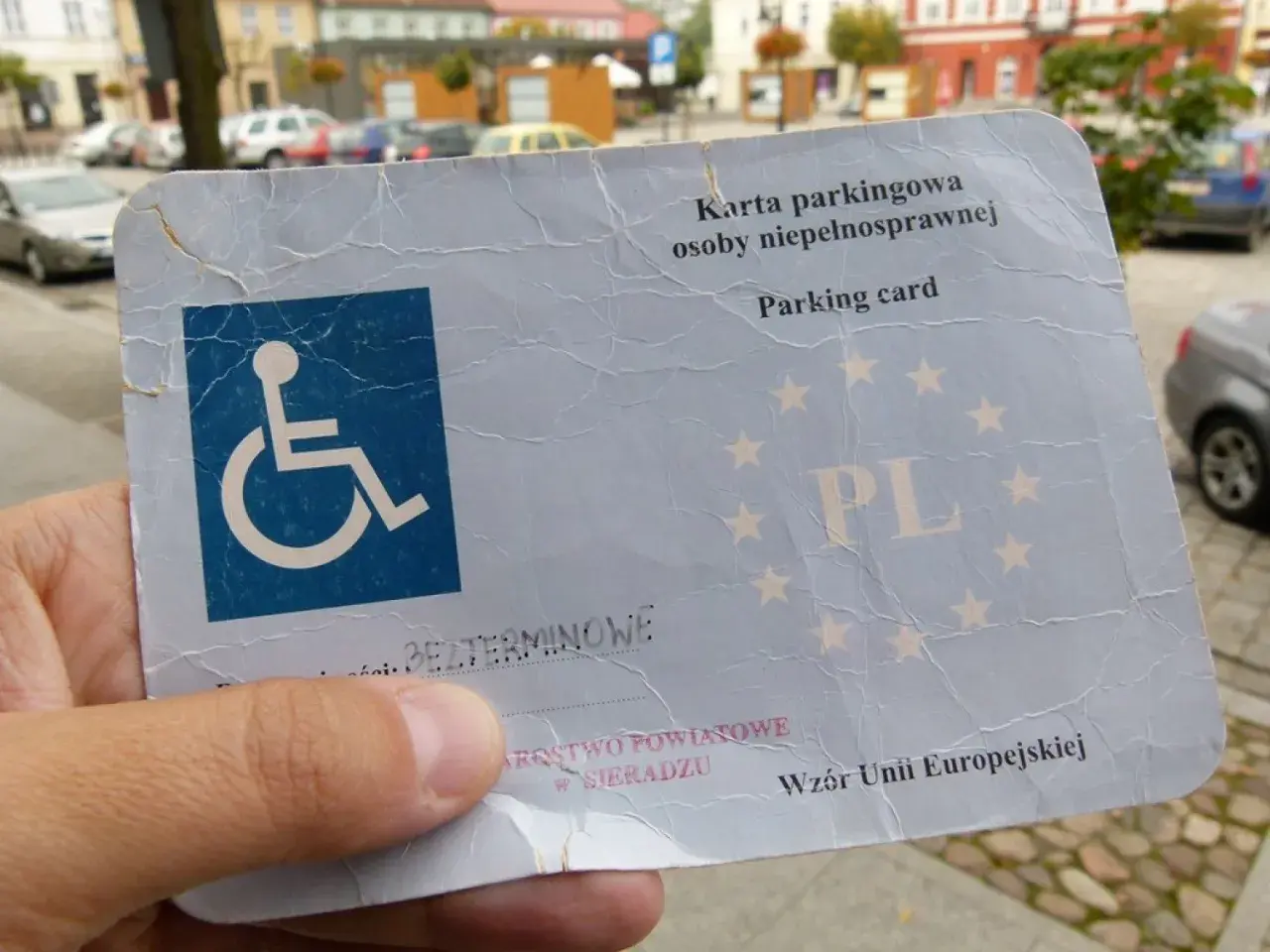 Karta parkingowa dla niepełnosprawnych, z symbolem wózka inwalidzkiego i oznaczeniem PL. Dokument wydany w Sieradzu, wzór Unii Europejskiej.