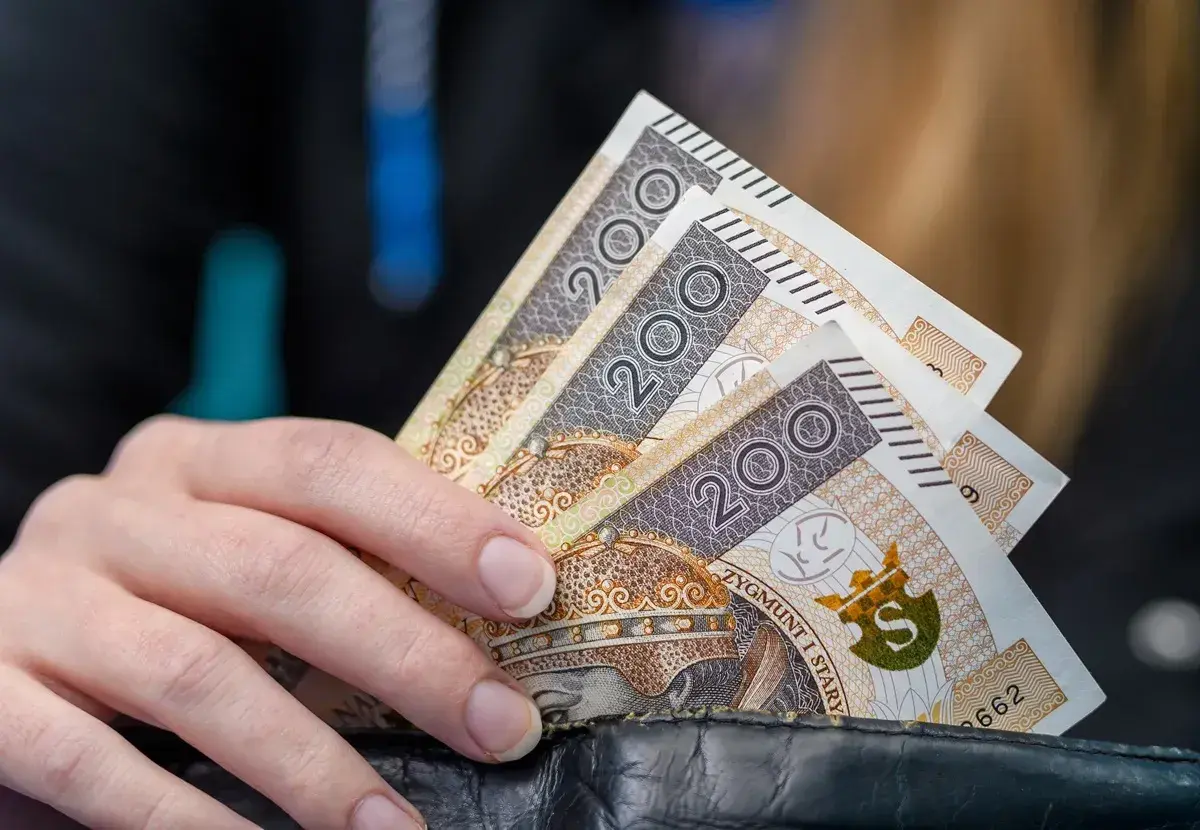 Dłoń trzyma banknoty 200 zł. Kto nie ma prawa do zasiłku dla bezrobotnych, musi radzić sobie sam.