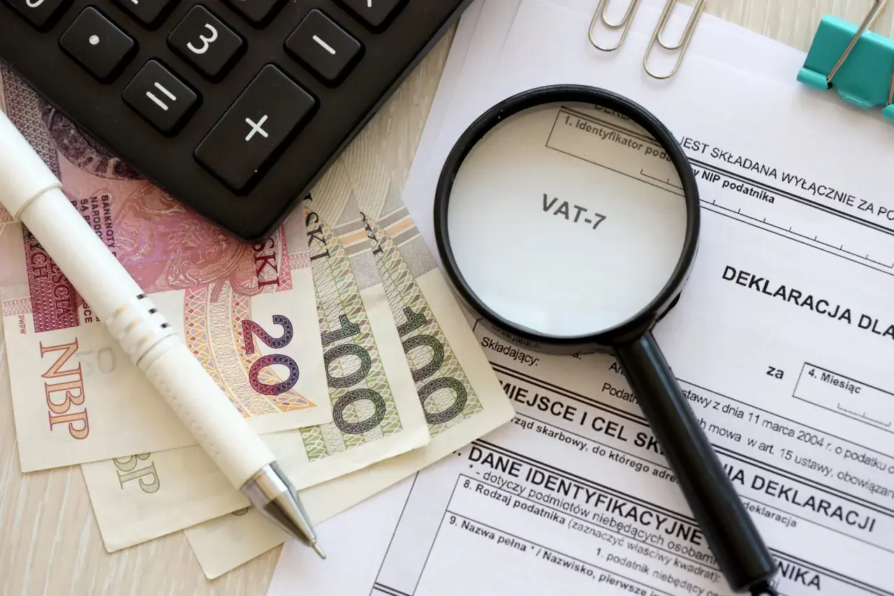 Pióro, banknoty, kalkulator i lupa nad deklaracją VAT-7. Przygotowanie do rozliczenia podatku.