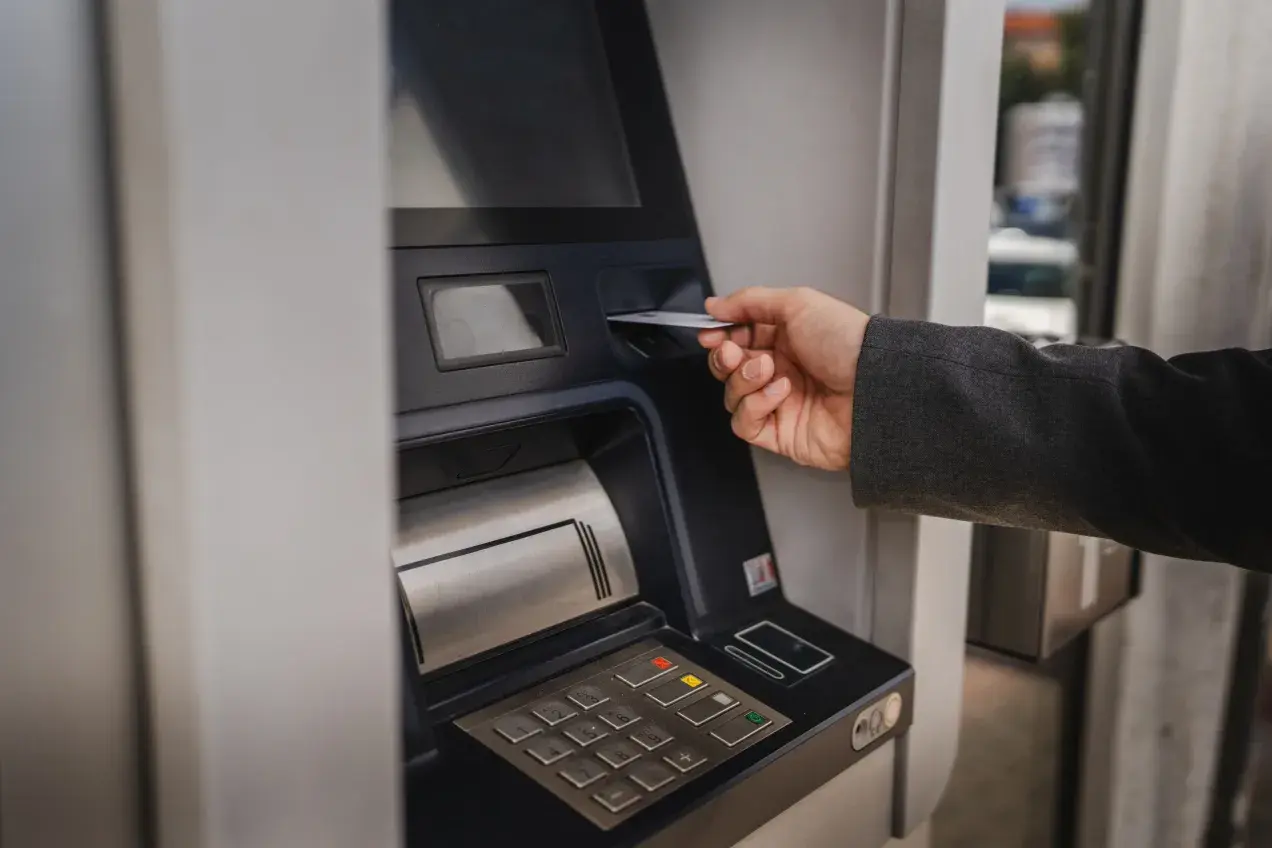 Dłoń wsuwa kartę do bankomatu, by sprawdzić, ile można wypłacić.