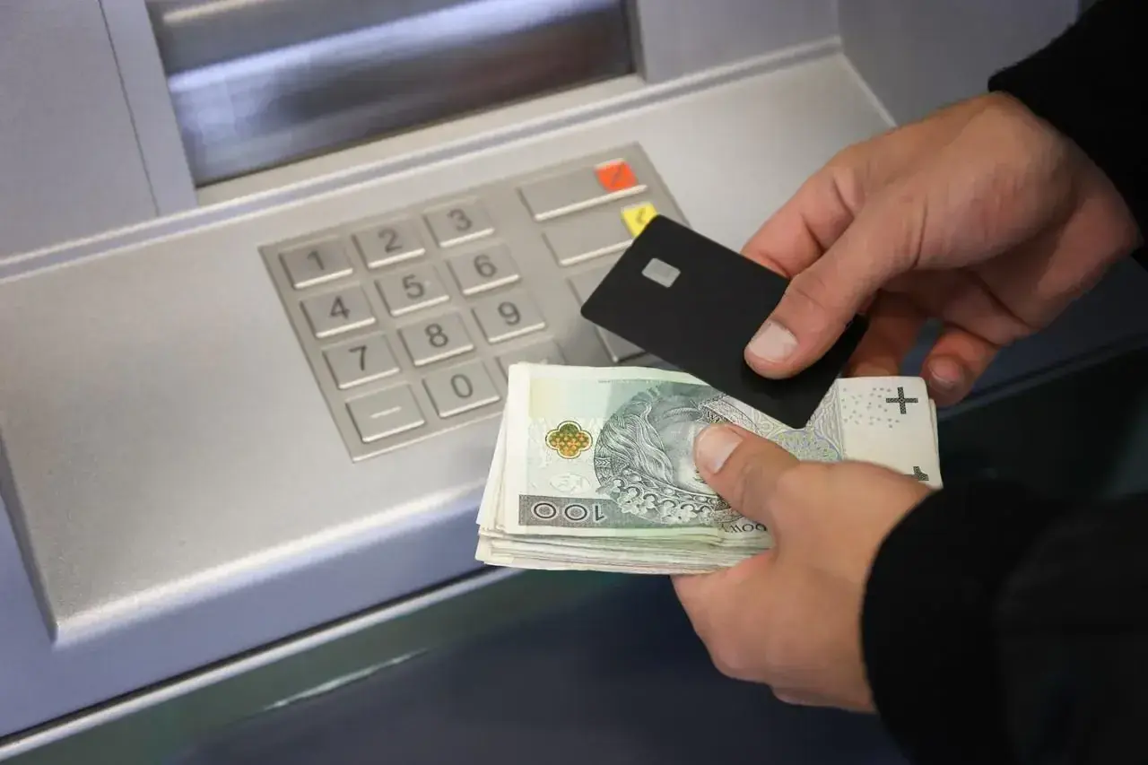 Ręce trzymające kartę i banknoty przy bankomacie. Dowiedz się, jak wpłacić pieniądze na konto.