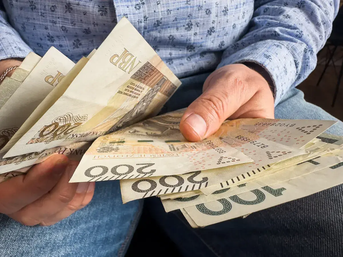 Ręce trzymające polskie banknoty 100 i 200 zł. Czy 800 plus wlicza się do dochodu?