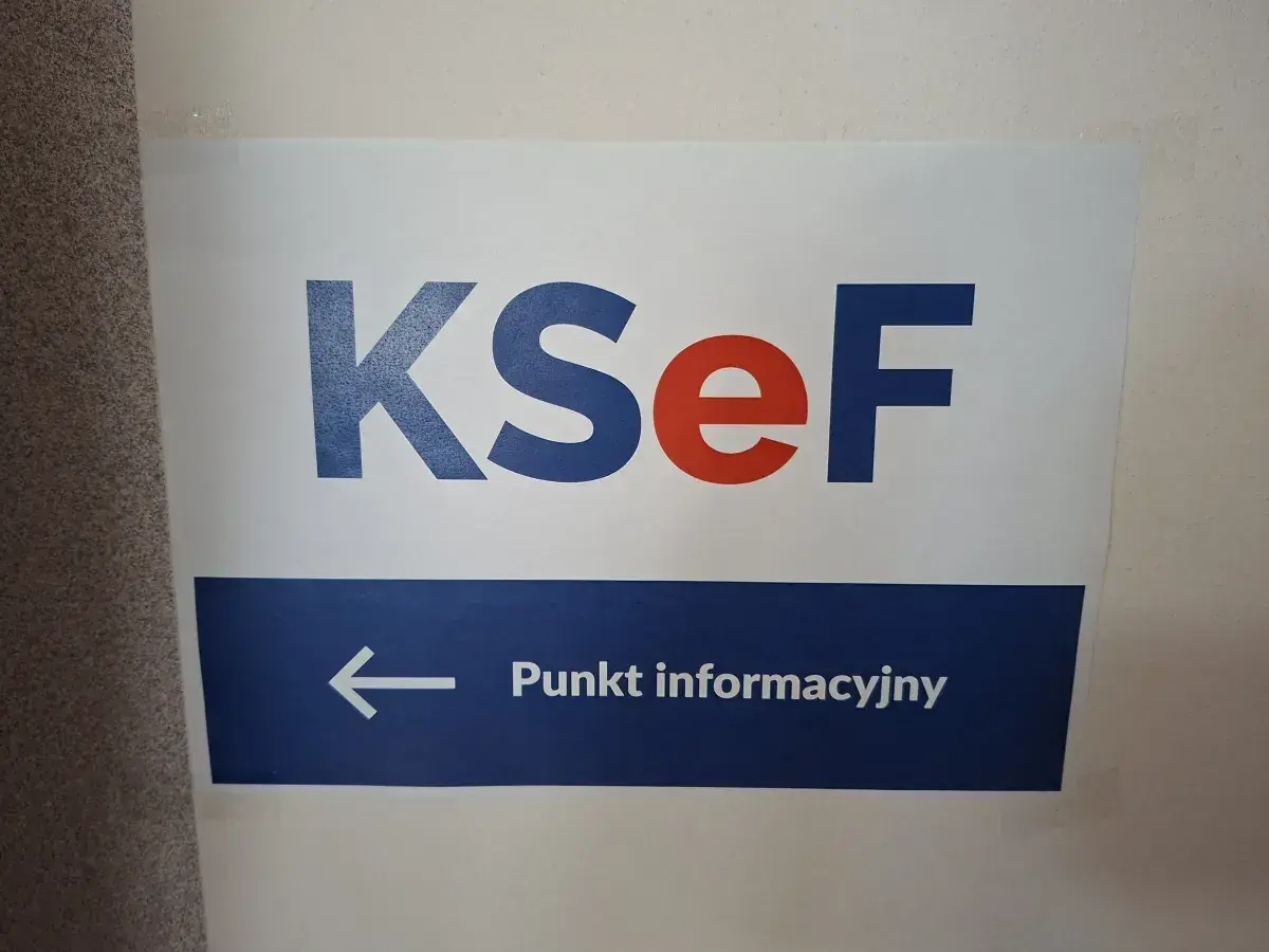 Tablica informacyjna KSeF. Strzałka w lewo wskazuje punkt informacyjny, gdzie można uzyskać pomoc podczas szkolenia.