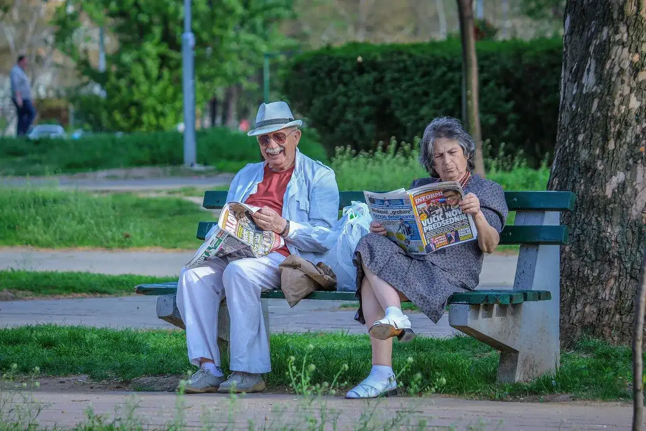 Starsza para, jak spółka partnerska, czyta gazety na ławce w parku.