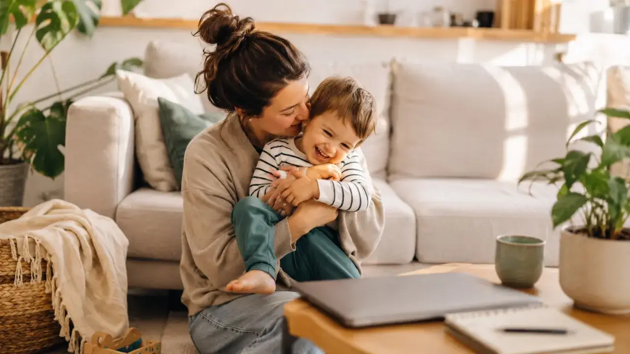 Mama na urlopie wychowawczym tuli roześmiane dziecko. Czas spędzony razem jest bezcenny.