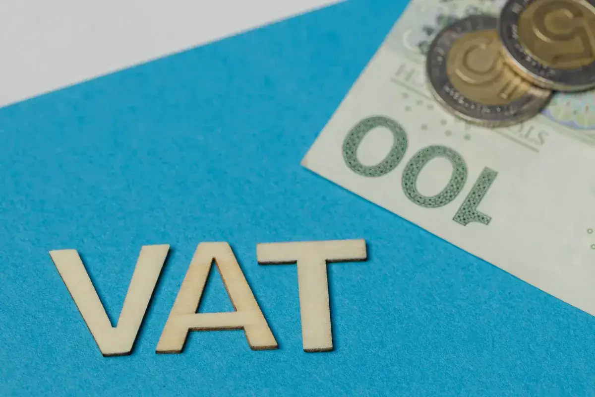 Drewniane litery VAT i banknot 100 zł z monetami. Temat związany z art. 113 ust. 1 ustawy o VAT.