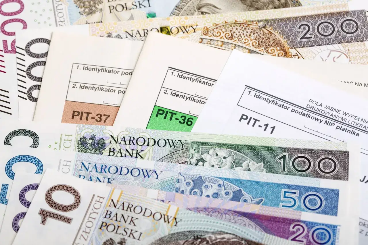 Formularze PIT-37, PIT-36, PIT-11 leżą na stosie polskich banknotów. Czas na rozliczenie i ulga na złe długi!