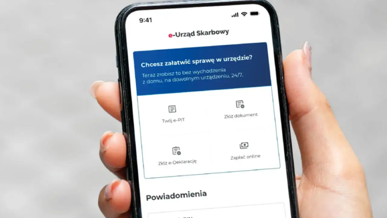 Dłoń trzyma smartfon z aplikacją e-Urząd Skarbowy. Można tu złożyć e-PIT, dokument, e-Deklarację lub zapłacić online.