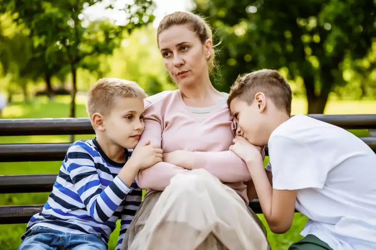 Samotna matka z dwoma synami na ławce w parku. Dzieci przytulają się do niej, szukając pocieszenia. To może być obrazek ilustrujący rozliczenie osoby samotnie wychowującej dziecko przykład.