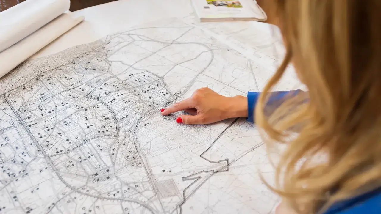 Kobieta analizuje mapę, wskazując palcem obszar, który może dotyczyć służebności.
