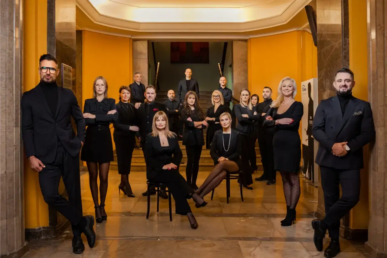 Grupa profesjonalistów w czarnych strojach pozuje w eleganckim wnętrzu.