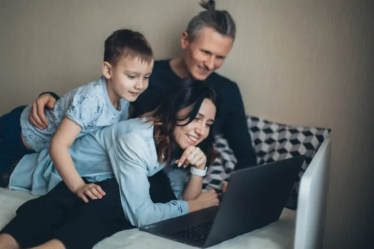 Rodzina ogląda coś na laptopie. Chłopiec siedzi na mamie, która leży, a tata stoi za nimi. To ich wspólna darowizna od rodziców.