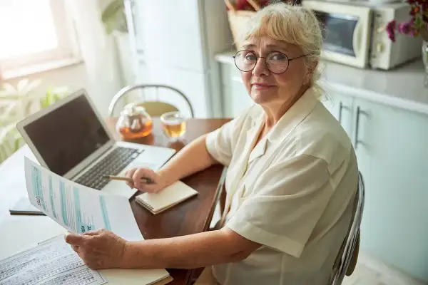 Kobieta z okularami analizuje dokumenty, planując emeryturę za 4 dzieci. Na stole laptop, herbata i notatnik.