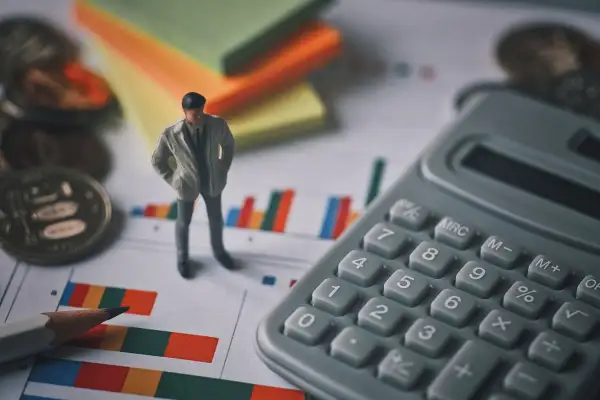 Figurka mężczyzny, kalkulator, monety i wykresy. Czy to syndyk, kto to? Analiza finansowa.