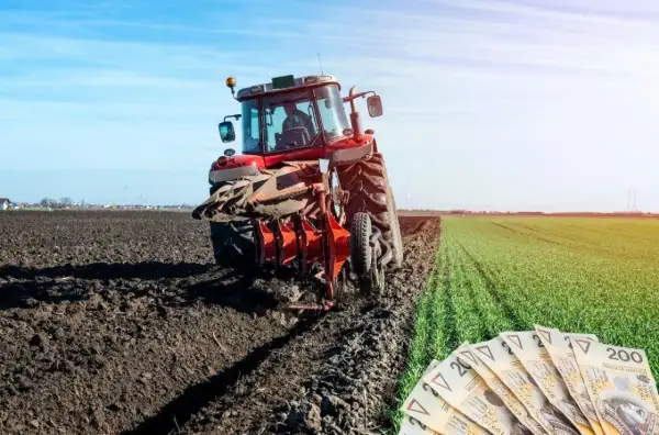 Czerwony traktor orze pole, a obok leżą polskie banknoty. Rolnicy liczą na to, że wzrosną wynagrodzenia w KRUS.