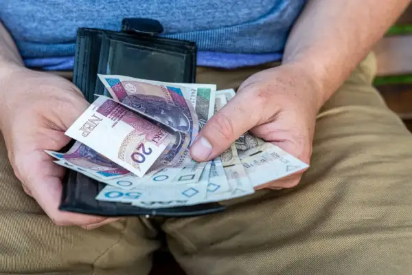 Dłonie trzymają portfel z polskimi banknotami. To może być świadczenie przedemerytalne, które zapewnia stabilność finansową.