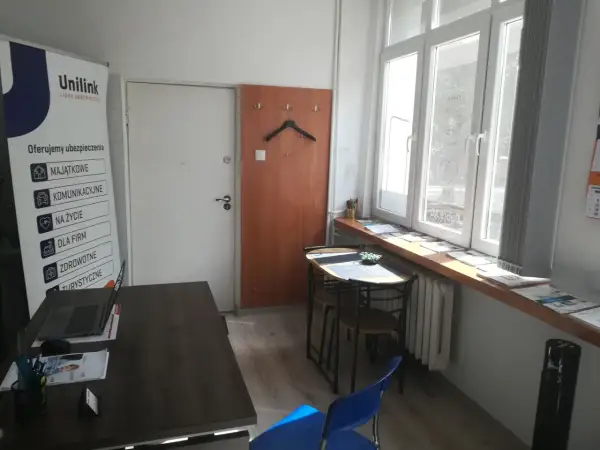 Biuro Unilink z banerem informacyjnym, biurkiem z laptopem i oknem.