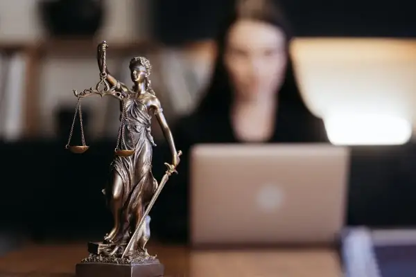 Figurka Temidy symbolizuje sprawiedliwość w sprawach o wydziedziczenie a zachowek. Kobieta pracuje przy laptopie.