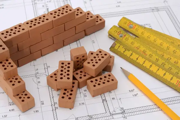 Miniaturowa budowa na planie architektonicznym: cegły, miarka i ołówek. To jakby planistyczna zabawa w budowanie.