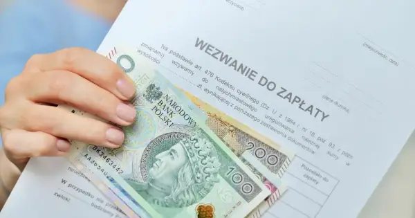 Dłoń trzyma banknoty 100 i 200 zł na wezwaniu do zapłaty. Zastanawiasz się, ile zarabia komornik?