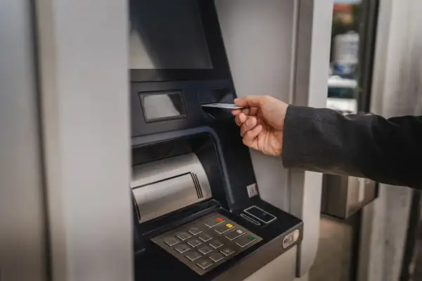 Dłoń wsuwa kartę do bankomatu, by sprawdzić, ile można wypłacić.