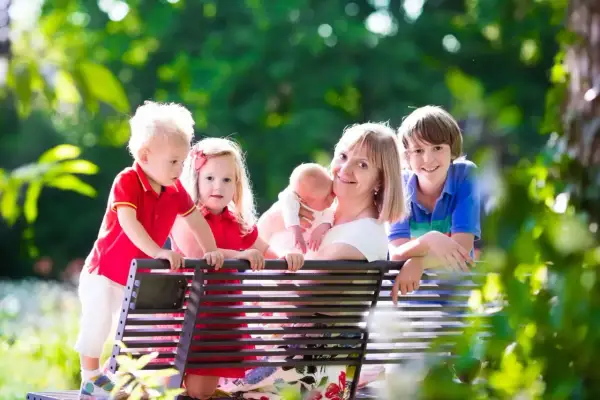 Szczęśliwa mama z czwórką dzieci na ławce w parku. Marzy o tym, kiedy emerytura dla matek 3 dzieci od kiedy będzie jej przysługiwać.