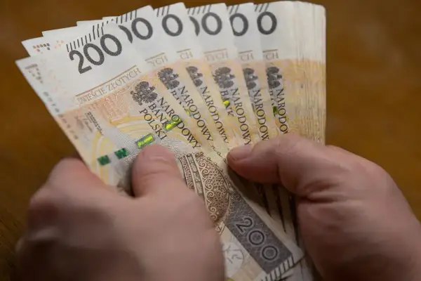 Dwie ręce trzymają plik banknotów po 200 zł. To może być wypłata 5000 brutto.