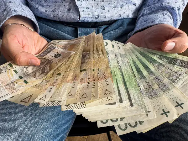 Ręce trzymające stos banknotów 100 i 200 zł. To darowizna od rodziców na nowy cel.