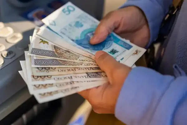 Ręce trzymają polskie banknoty. Czy to dodatek do emerytury za urodzenie 2 dzieci?