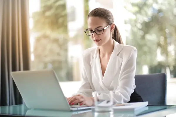 Kobieta w okularach pracuje na laptopie, planując swoją nierejestrowaną działalność gospodarczą.