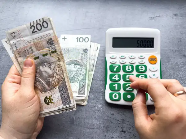Ręka trzyma banknoty 200 zł i 100 zł, obok kalkulator z wyświetloną kwotą 50000. Czy to prognoza wynagrodzenia minimalnego 2026?