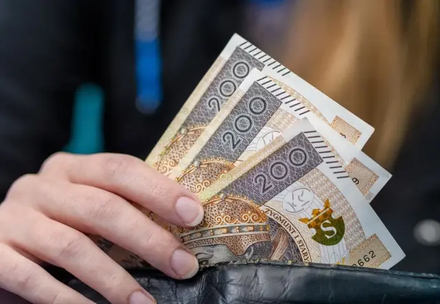 Dłoń trzyma banknoty 200 zł. Kto nie ma prawa do zasiłku dla bezrobotnych, musi radzić sobie sam.
